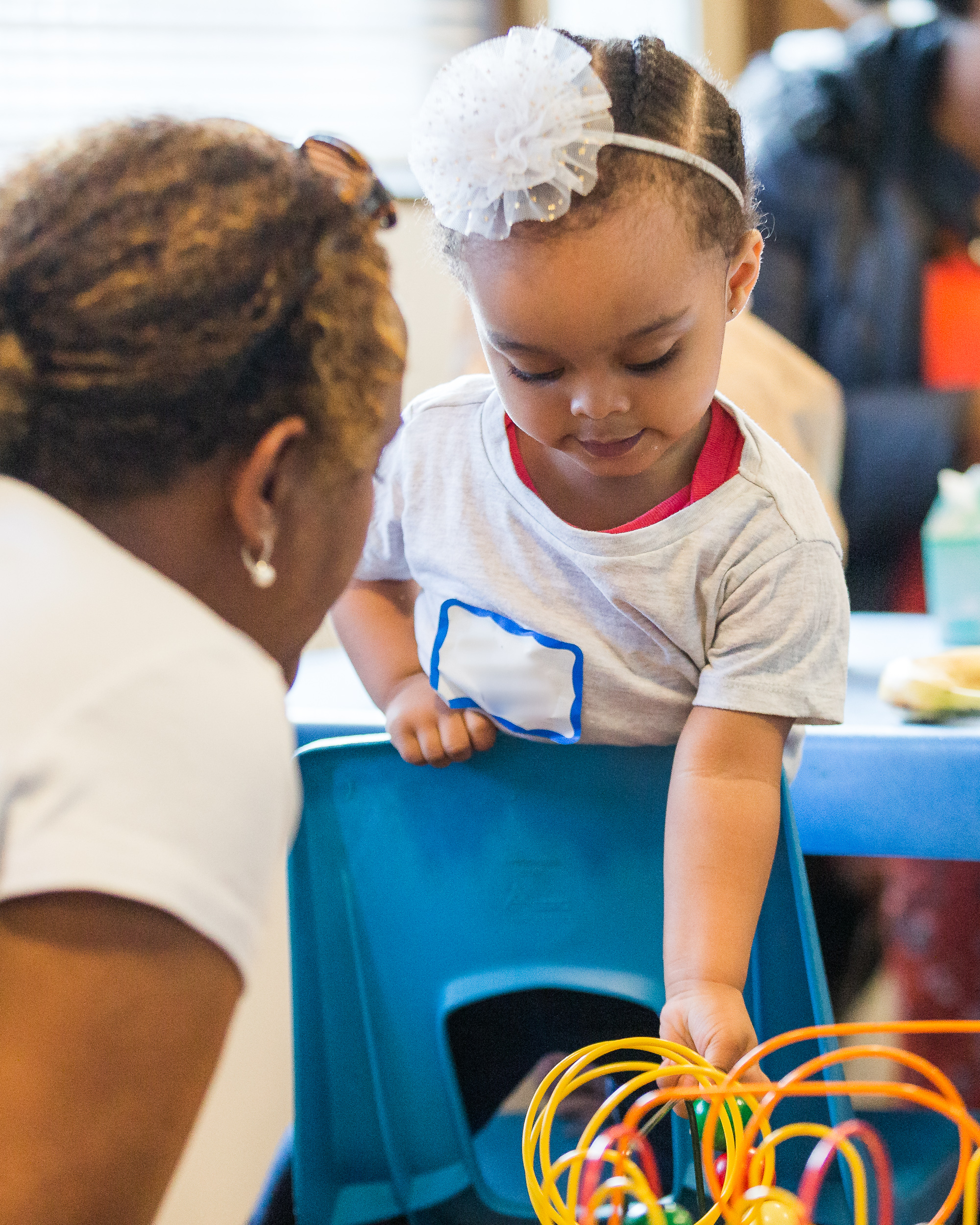 woman looking at a child leaning over a chair and playing with a wire toy