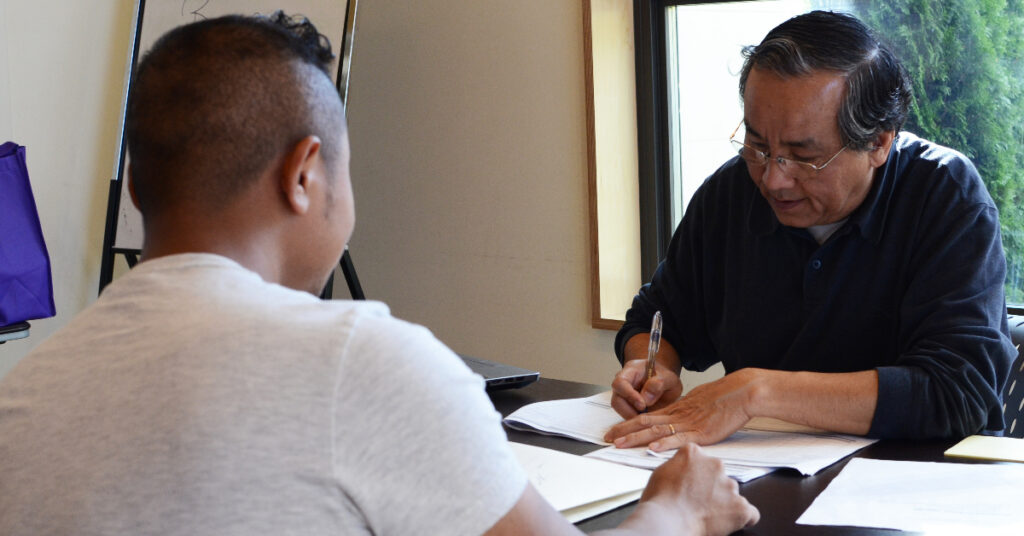 Two men across from each other at a table going over paperwork