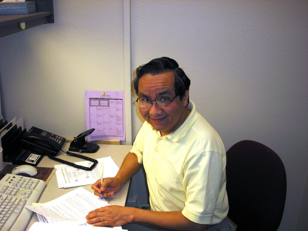 Man sitting at his desk writing but looking up and smiling