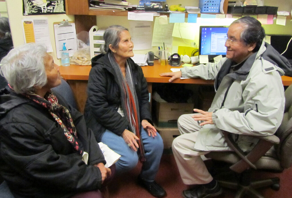 Three people talking to each other on one side of the desk.