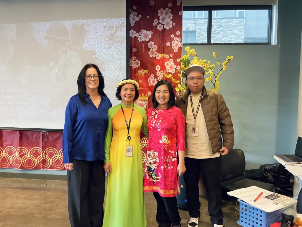 Four people dressed in traditional Vietnamese clothing in front of a decorated wall.